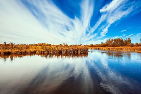 Cirrus clouds are reflected in the Winnipeg River. Wonderful autumn day in Manitoba. Old Pinawa Dam