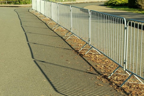 Metal crowd control barriers casting long shadows on an asphalt road
