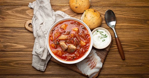 Ukrainian Borscht, red beetroot soup with meat, in white bowl with sour cream, garlic buns