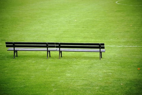 A trainer's bench stands at the edge of a football pitch in a football stadium