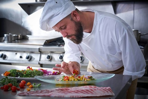 Chef garnishing flower in ceviche dish with hands at stainless steel kitchen