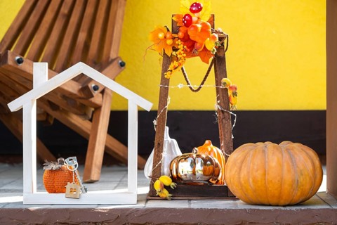Autumn decor on porch of yellow house outside of pumpkin, lantern, garlands and figure of home and