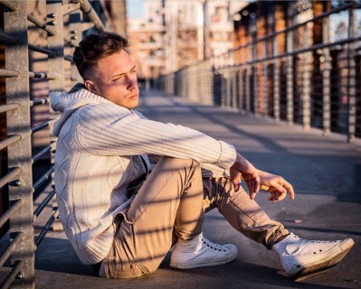 Handsome trendy young man, sitting in city setting at sunset wearing a fashionable sweater or