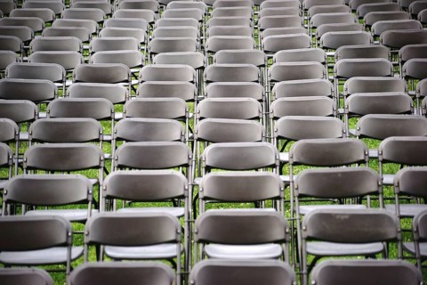 Parallel rows of empty folding chairs in a meadow in front of a concert