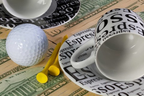 Two empty coffee cups and golf equipments lying on US dollar banknotes
