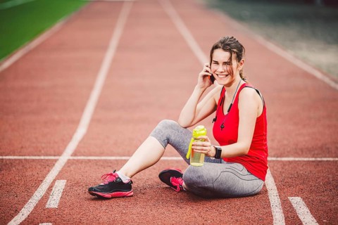Sport and technology. A beautiful young Caucasian woman with ponytail sitting resting after workout
