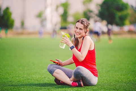 Theme sport health. beautiful young girl sitting resting on green grass lawn stadium using