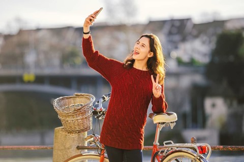 A beautiful young woman with a retro red bicycle is making a photo of herself in the old city of