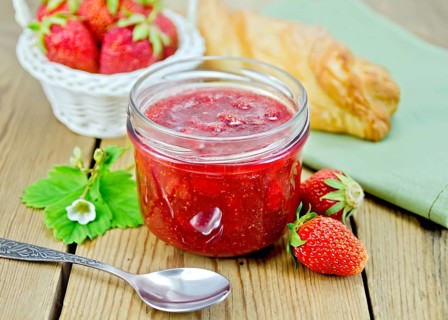 Strawberry jam in a glass jar, layered bun, strawberry, napkin, spoon on a wooden boards background