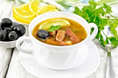 Soup saltwort with lemon, meat, pickles, tomato sauce and olives in a white bowl, towel, parsley on