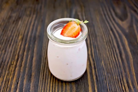 Yogurt with strawberries in a glass jar on a wooden boards background