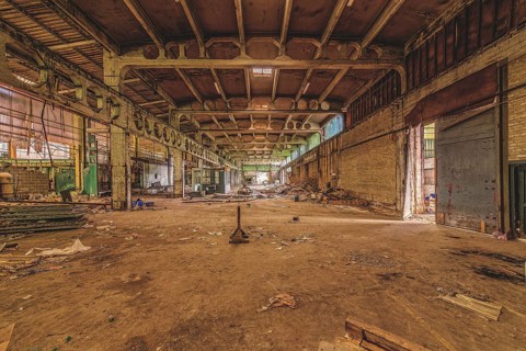 Wide, abandoned factory hall with debris on the floor and visible ceiling construction, The
