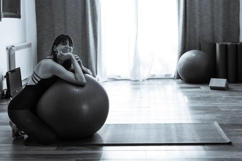 A woman leaning on a fitness ball while she looks at the camera