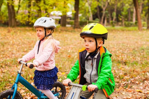 Portrait of screaming preschool girl in protective helmet riding balance bike outdoors at the park.