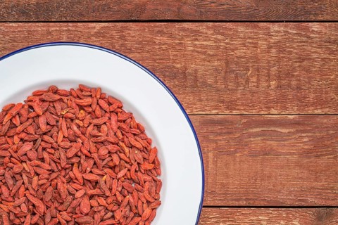 Dried goji berries on white metal enamel plate against rustic wood, top view with a copy space
