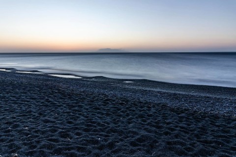 Morning atmosphere, sunrise over the sea, view from the lava beach to the island of Anafi, long