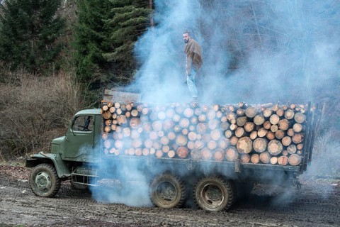 Young man on vintage truck with logs in the forest