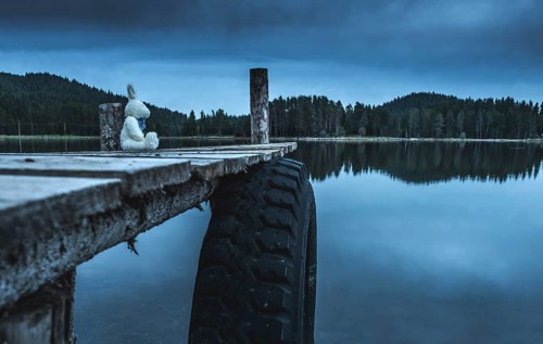 Fluffy toy bunny sitting on a pier. Shore of a mountain lake