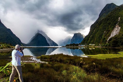 New Zealand. The famous ocean fjord Milford Sound. The gray-haired tourist photographs a