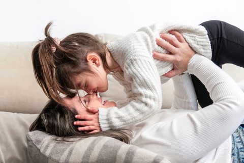 Mom and daughter are lying on the sofa, wearing white sweaters, sharing a tender moment of love and