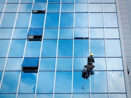 Window cleaner working on a glass facade suspended. Heavy work concept