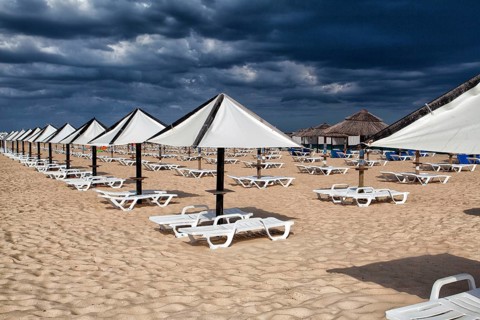 Different parasols and sun loungers on the empty beach on Tavira island before storm, Algarve.