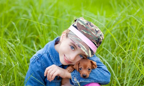 Little girl with pet puppy mascot mini pinscher in outdoor green grass