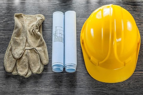 Safety gloves blueprints hard hat on wooden board