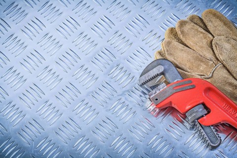 Pair of protective gloves pipe wrench on fluted metal sheet construction concept