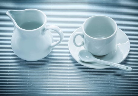 White ceramic cup saucer teaspoon creamer on striped background