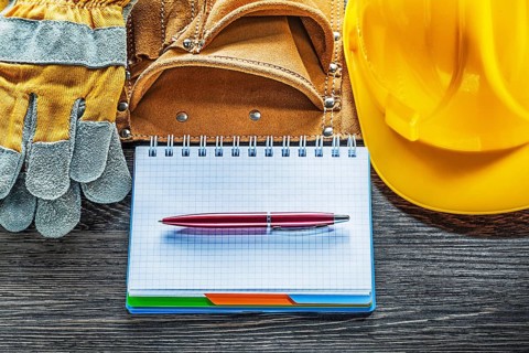 Notepad pen tool belt safety gloves hard hat on wooden board