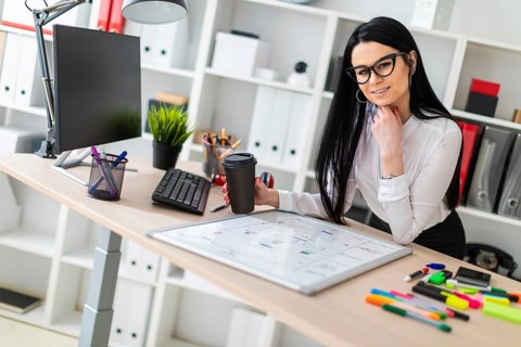 A young girl with glasses, wearing a white blouse and black trousers, works in the office. The girl