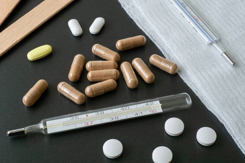 Traditional medical thermometer for measuring body temperature. Pills and medicaments on background