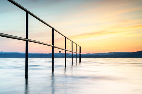 Railing in the lake at sunrise with gentle waves and peaceful sky, lido, Litzelstetten, Lake