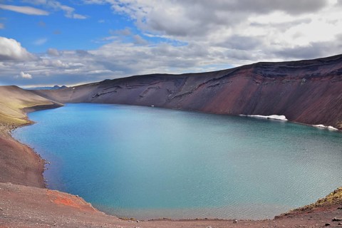 Oval blue lake in the crater of the volcano cooled down. Steep banks of the lake of red rhyolite.