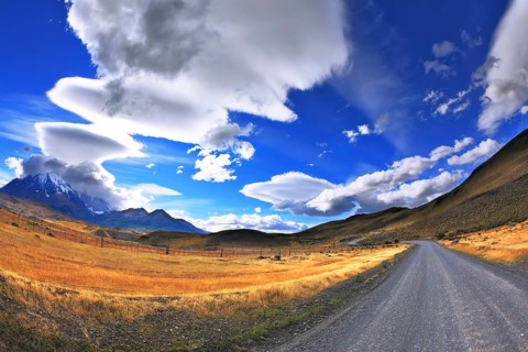 Gray dirt road in the Chile National Park Torres del Paine. Incredible shaped cloud formed by