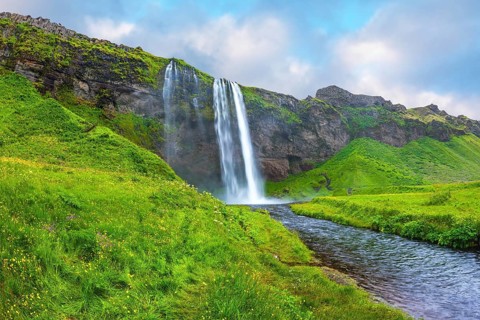 The warm July day in Iceland. Seljalandsfoss waterfall. Rainbow decorates drop of water