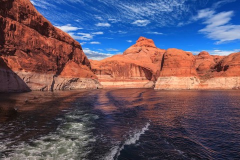 The foamy trace from powerboat crosses emerald waters. Hills from red sandstone surround the lake.