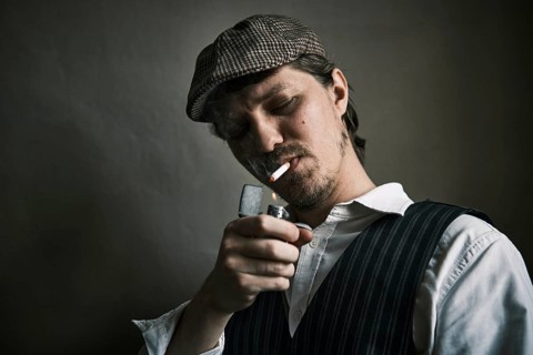 Young guy lights a cigarette, blows smoke, dressed in a retro style, in a beret, cinematic shot,
