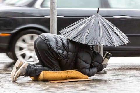 Homeless beggar is begging for money in a main street in Sofia holding an umbrella in a rainy day.