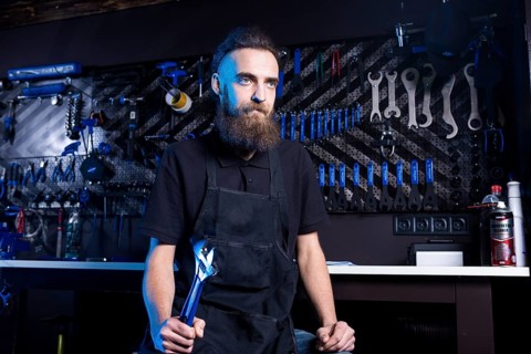 Portrait of small business owner of young man with beard. Guy bicycle mechanic workshop worker