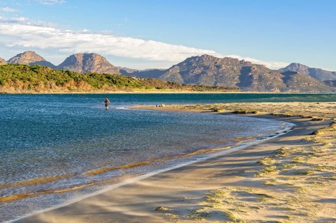 An angler in the shallow water on the Nine Mile Beach near Swansea with the Freycinet National Park