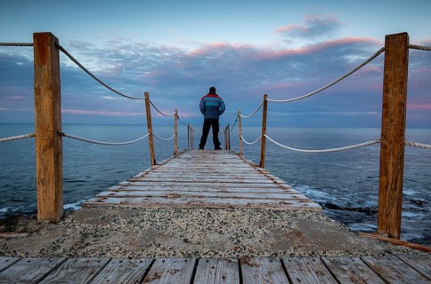 Person standing at the edge of a wooden pier in the sea at sunrise, People active outdoors enjoy