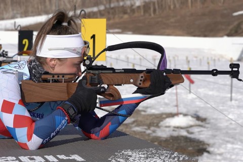 Sportswoman biathlete aiming, rifle shooting prone position. Biathlete Victoria Petrova Saint