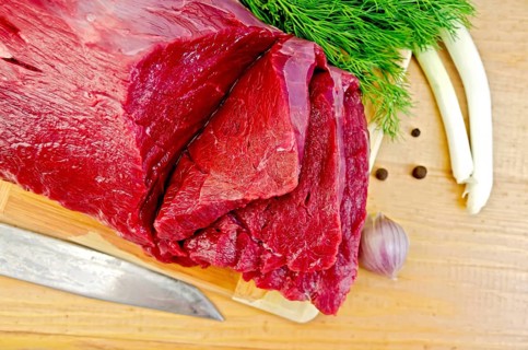 A piece of beef, garlic, peas pepper, dill, chives, knife on a wooden board