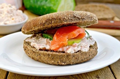 Sandwich of rye bread with cream, cucumber, dill and salmon on a plate on a wooden boards