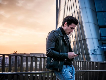 One handsome young man in urban setting in modern city, standing, wearing black leather jacket and