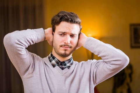 Handsome young man covering his ears, stressed or unhappy because of too much noise. Indoors shot