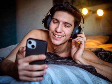 Glad male in headset smiling and text messaging on mobile while listening to favorite song and