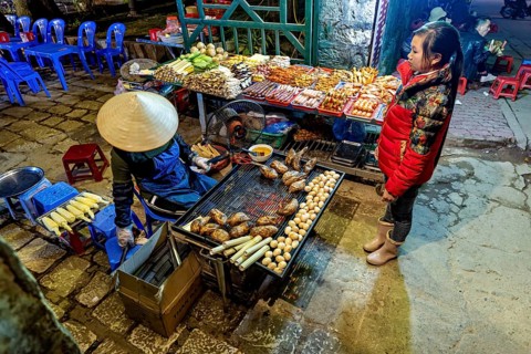 A busy street market with a stall selling grilled food surrounded by visitors, restaurant in the